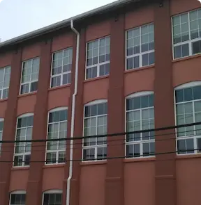 A three-story building with red brick walls and multiple large windows showcases expert roofing in Riverdale NJ. Black cables run horizontally across the lower part of the image, hinting at quality craftsmanship by a renowned roof company in Riverdale NJ.