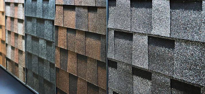 Close-up of several rows of asphalt roofing shingles in different colors and textures, displayed vertically in a showroom for comparison.