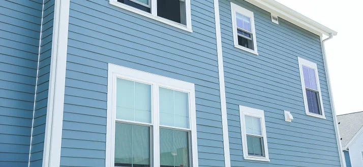 Blue house with white trim, featuring multiple windows on two stories. The siding is horizontal, and part of another house’s roof is visible on the right side of the image.